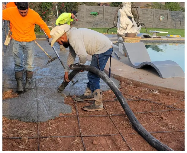 Workers pouring and leveling concrete at a construction site.