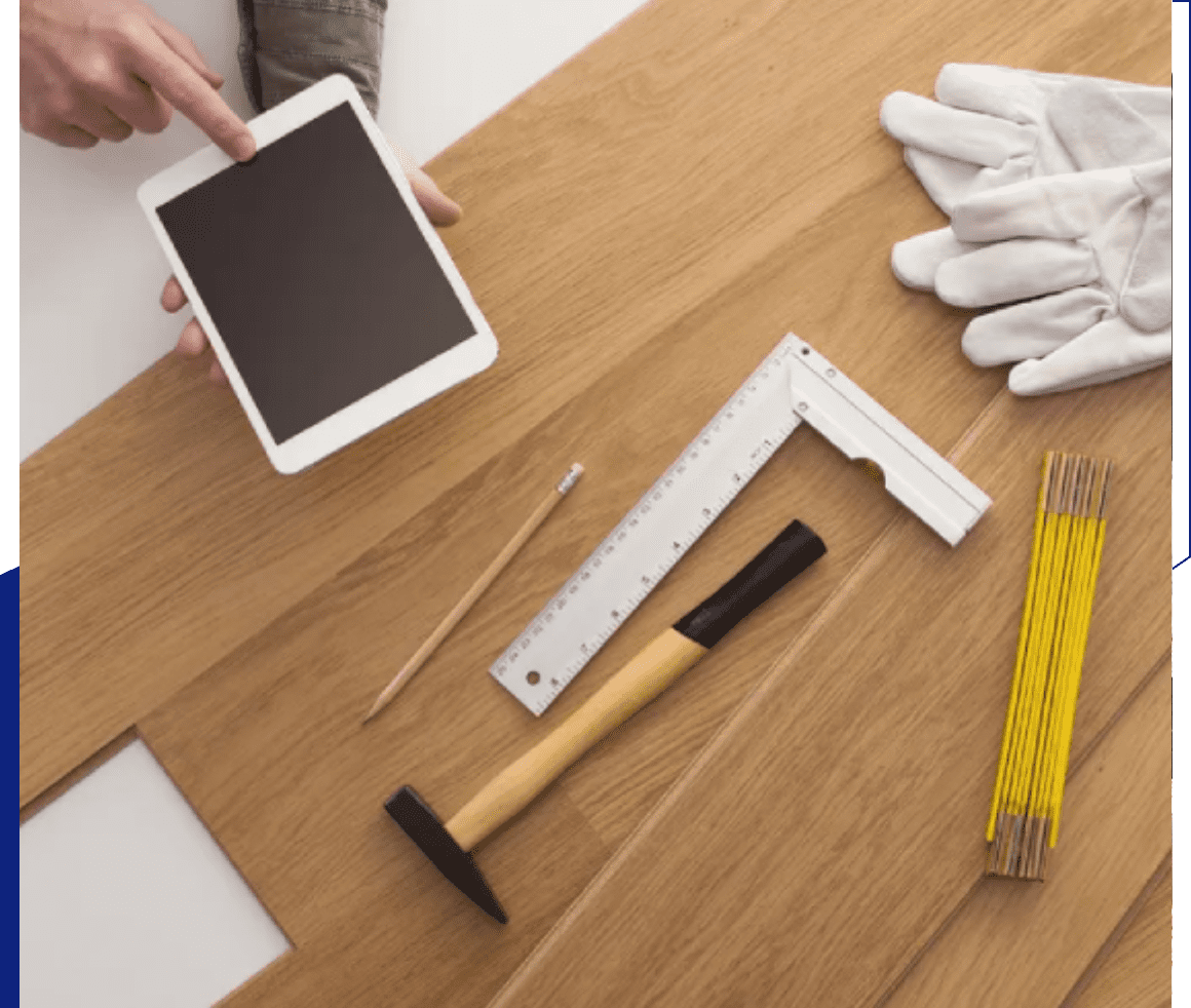 A wooden surface with a hammer, measuring tape, gloves, set square, and a pencil.